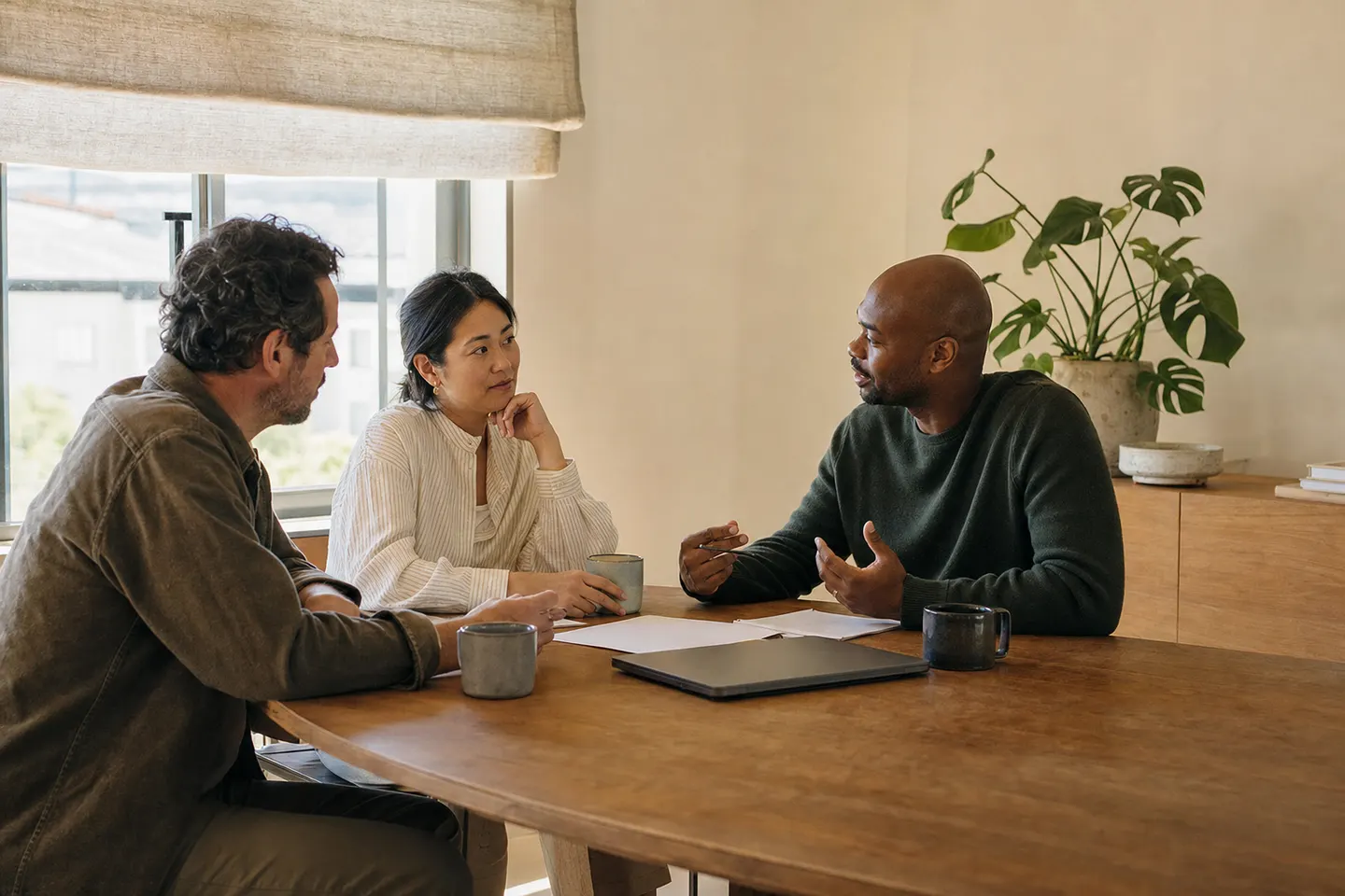 Three adults talking round one end of a plain meeting table with papers between them